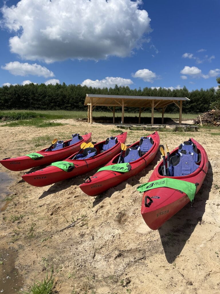 Kajaki na brzegu rzeki w Sudzinku przygotowane do spływu kajakowego Pilicą.